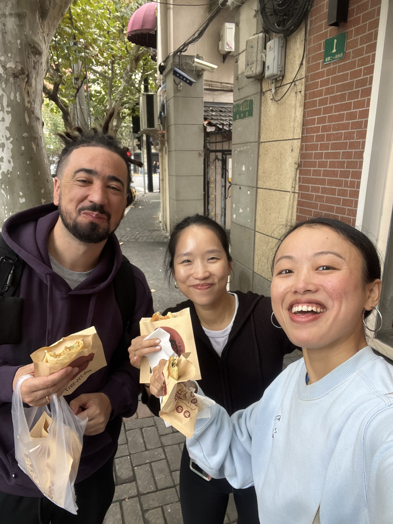 Three people enjoying Chinese pancakes together on a Shanghai street