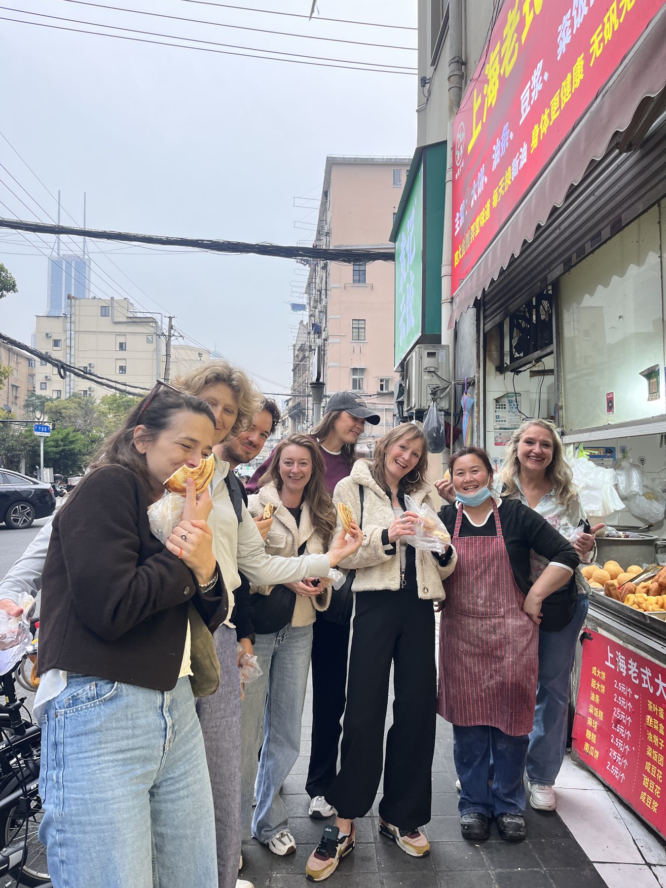 A group sharing local food beside a Shanghai street-food shop